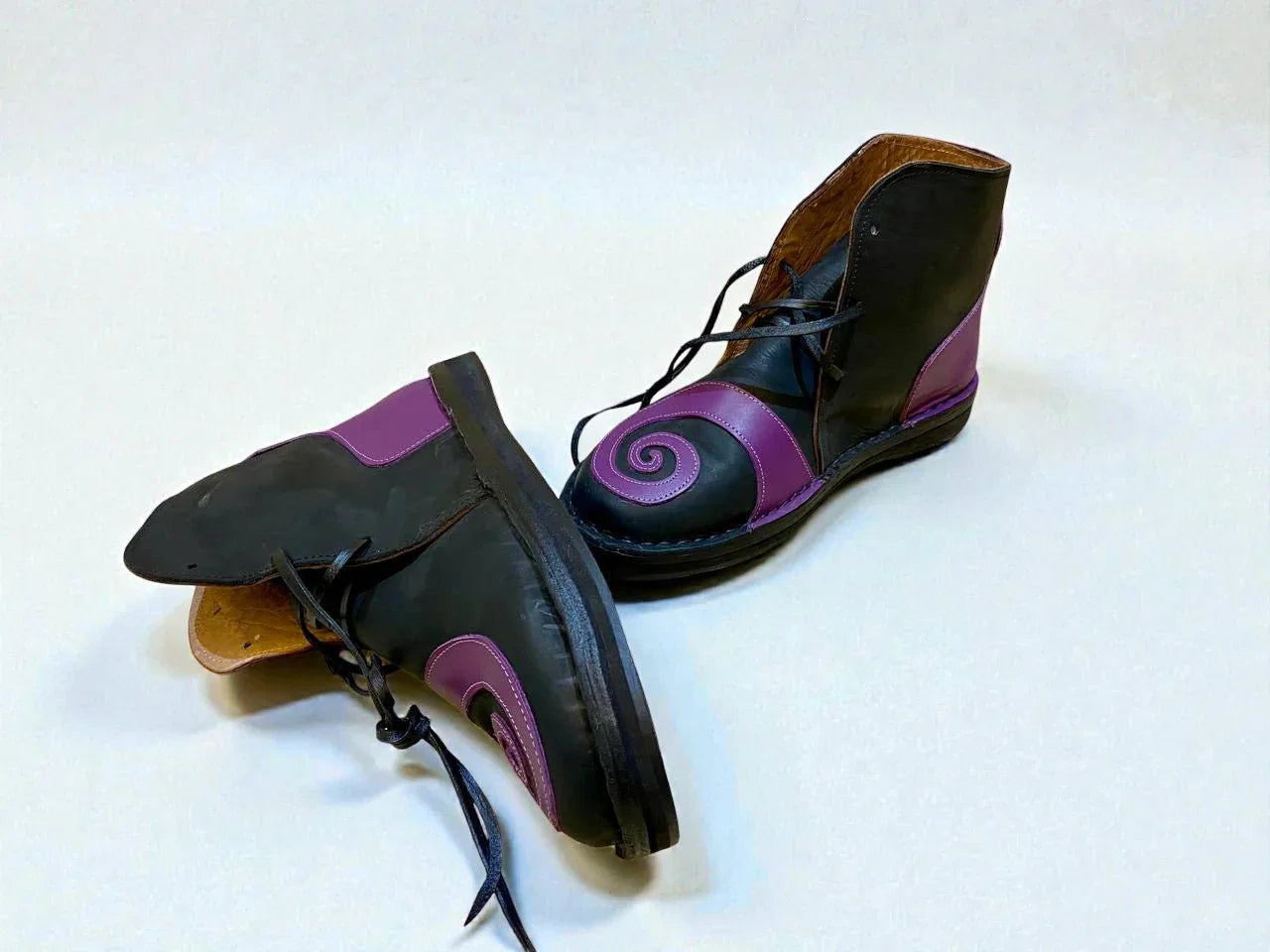 Black and purple handmade leather boots with spiral design, ideal for LARP or Renaissance faire events.
