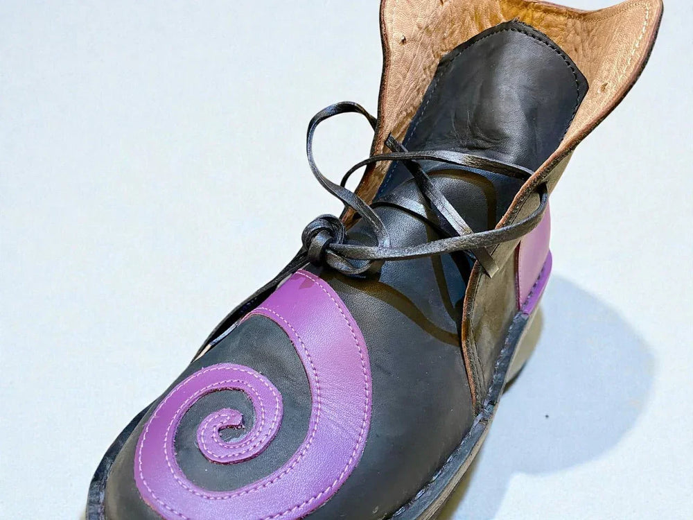Black and purple handmade leather boot with spiral design, wrap laces, and full-grain texture for Renaissance faire or LARP.
