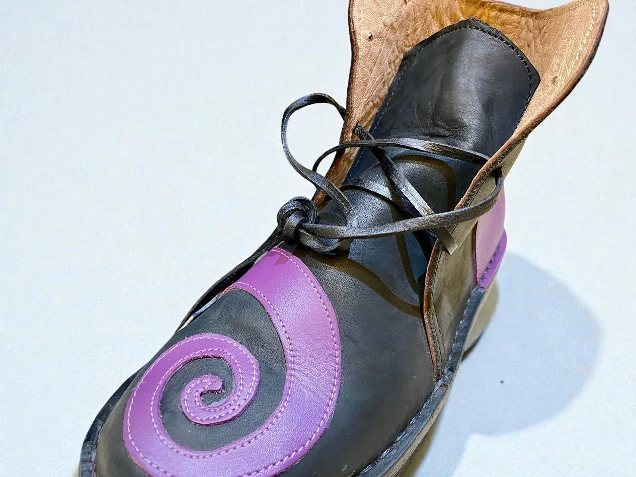 Black and purple handmade leather boot with spiral design, wrap laces, and full-grain texture for Renaissance faire or LARP.