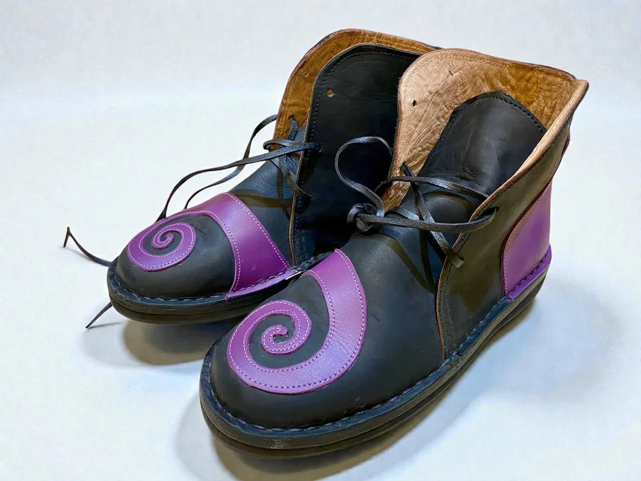 Handmade medieval leather boots with purple spiral design, black wrap laces, and full-grain leather texture for LARP or Renaissance faire.