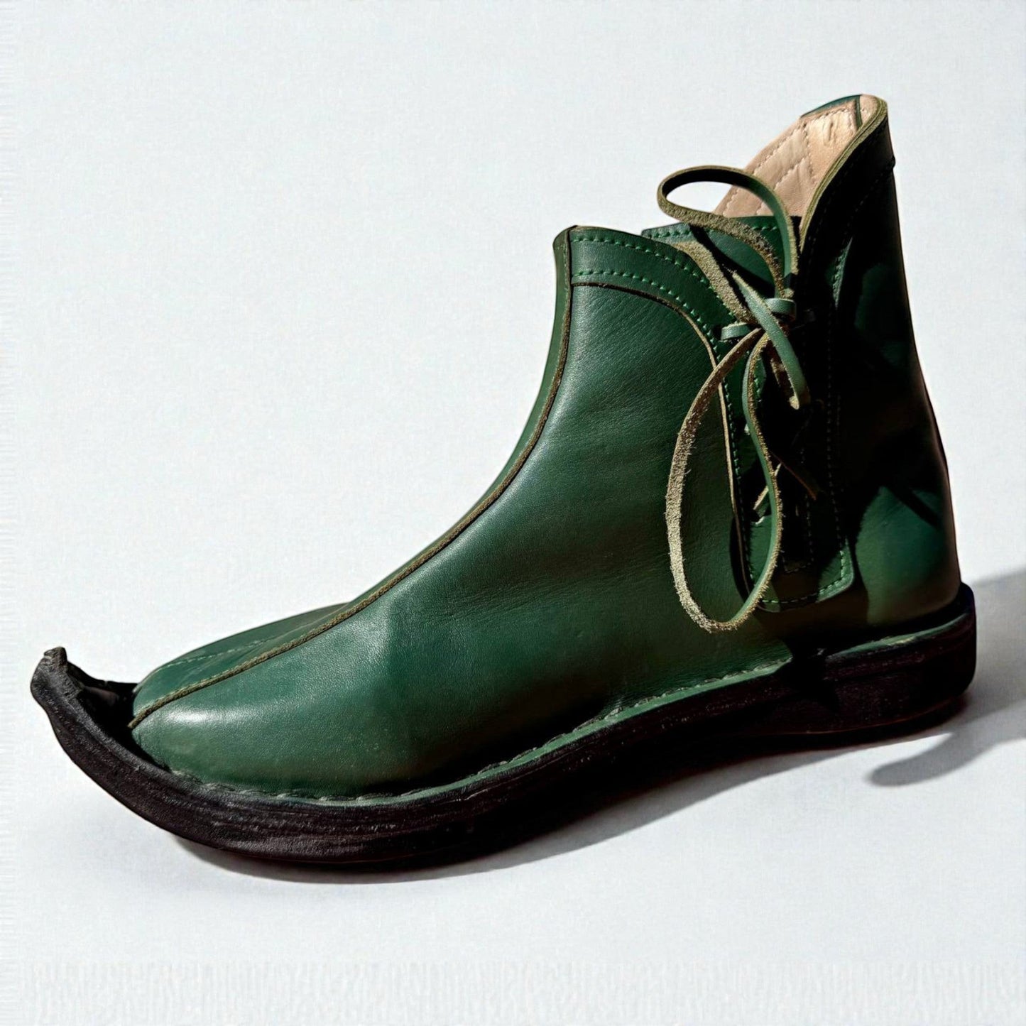 Handmade green medieval leather boot with wrap laces, visible stitching, and full-grain leather texture for LARP or SCA.