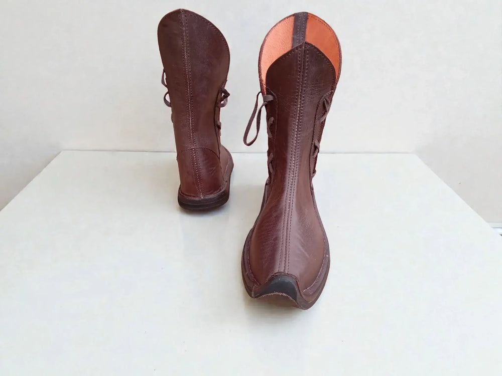 Handmade medieval leather boots with wrap laces, visible stitching, and full-grain leather texture on white background.
