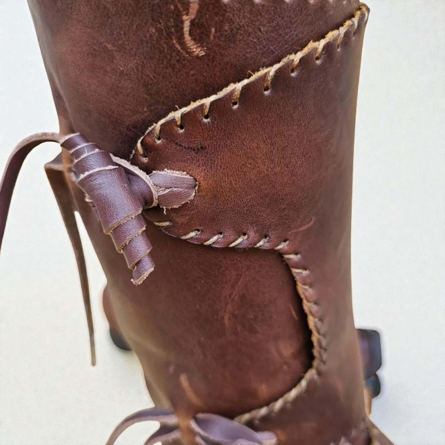 Close-up of handmade medieval leather boot with wrap laces and visible stitching, crafted from full-grain leather.