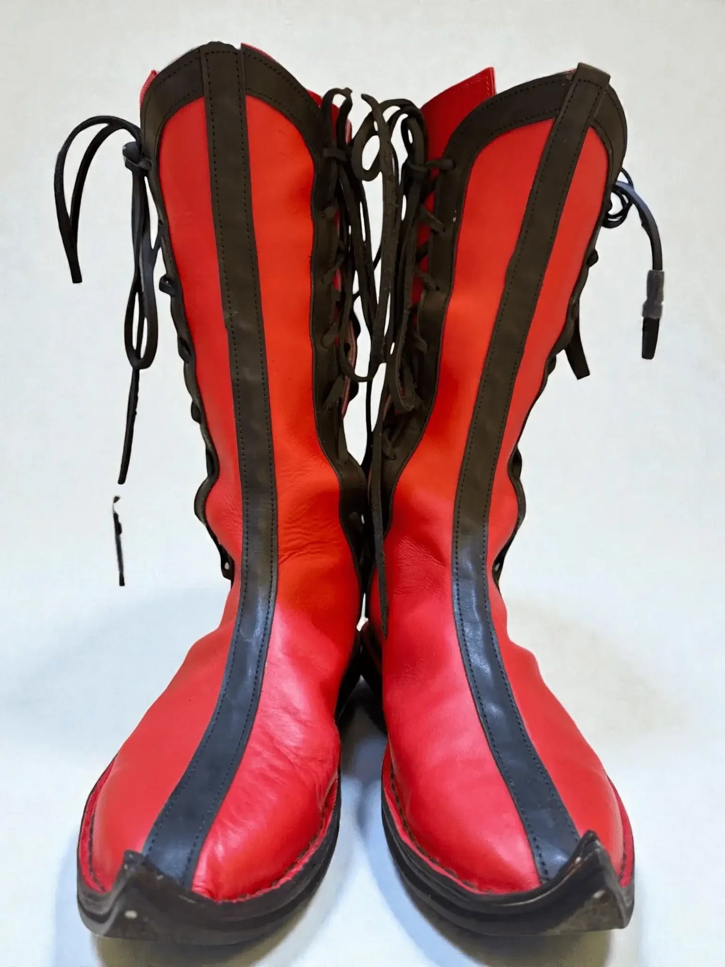 Vibrant red medieval leather boots with black side panels, wrap laces, and pointed toes, crafted for LARP or Renaissance faire.