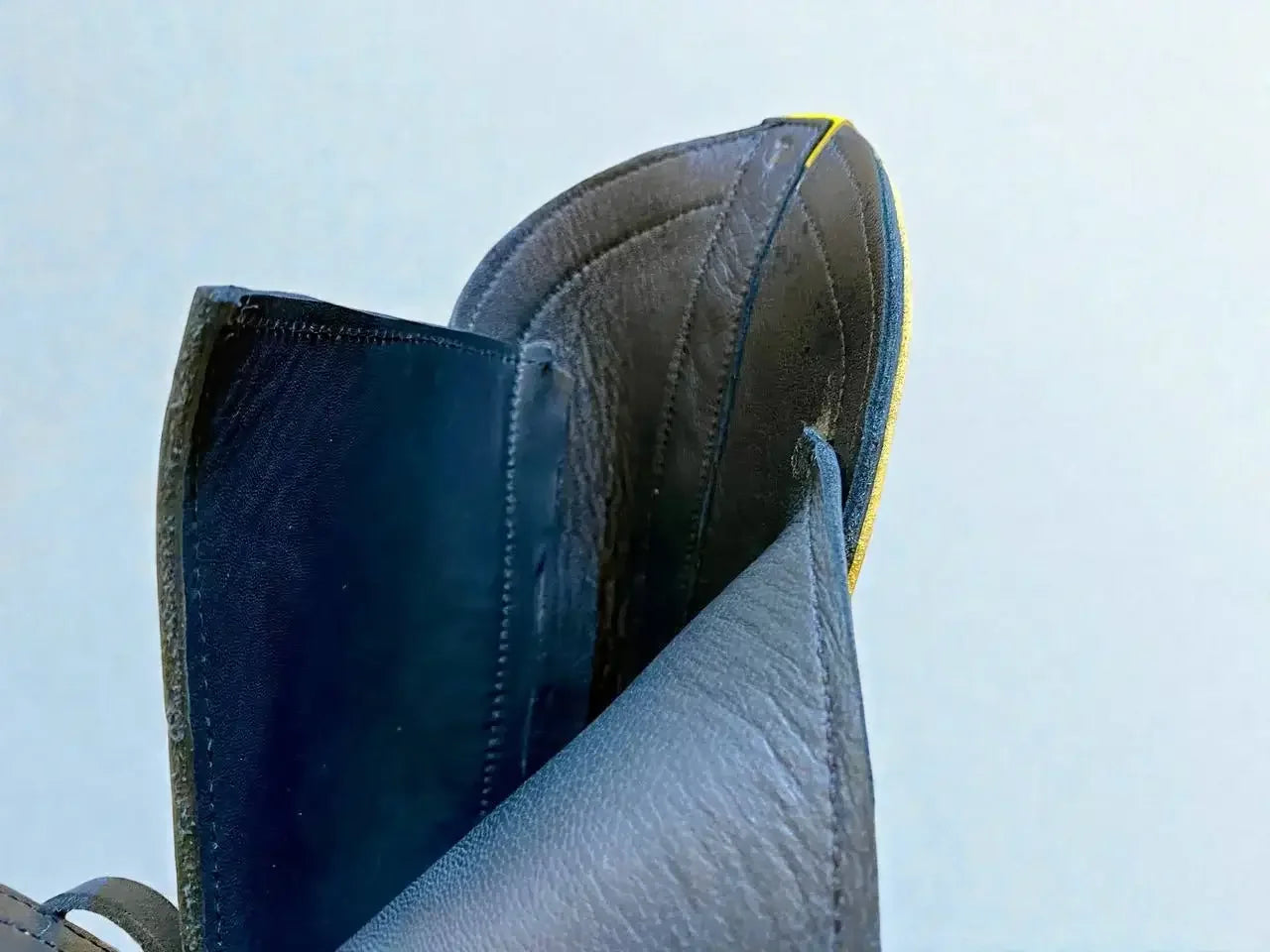 Close-up of handmade medieval leather boots showing full-grain texture, stitching, and yellow trim detail.