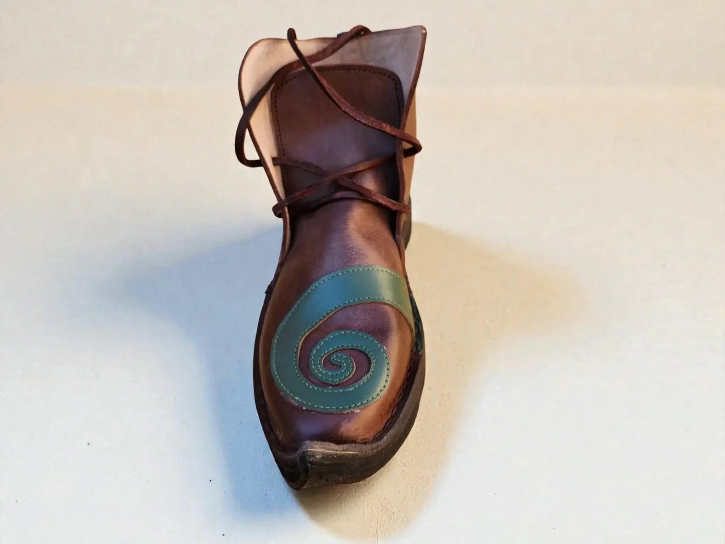 Handmade medieval leather boot with green spiral design, wrap laces, and full-grain texture for LARP or Renaissance faire.
